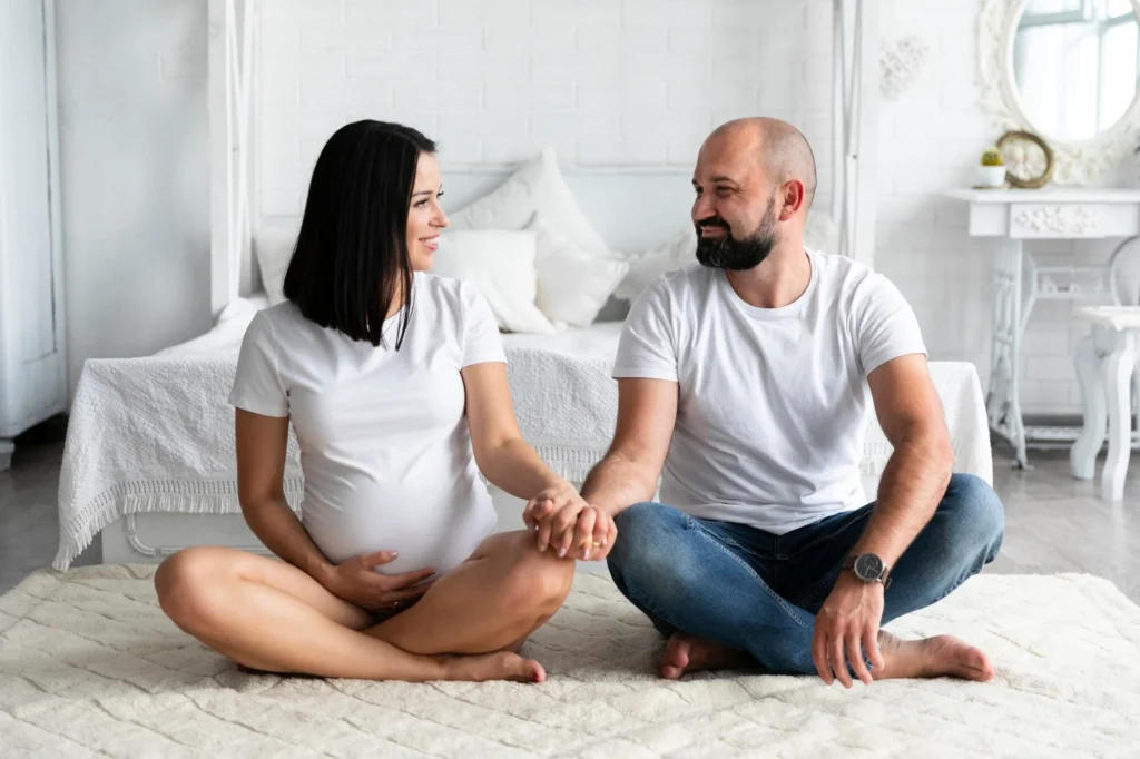 Pregnant woman sitting on the bedroom floor with her husband